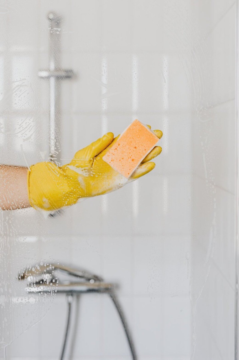 Ruka osobe koja čisti staklo tuš kabine u žutim gumenim rukavicama
