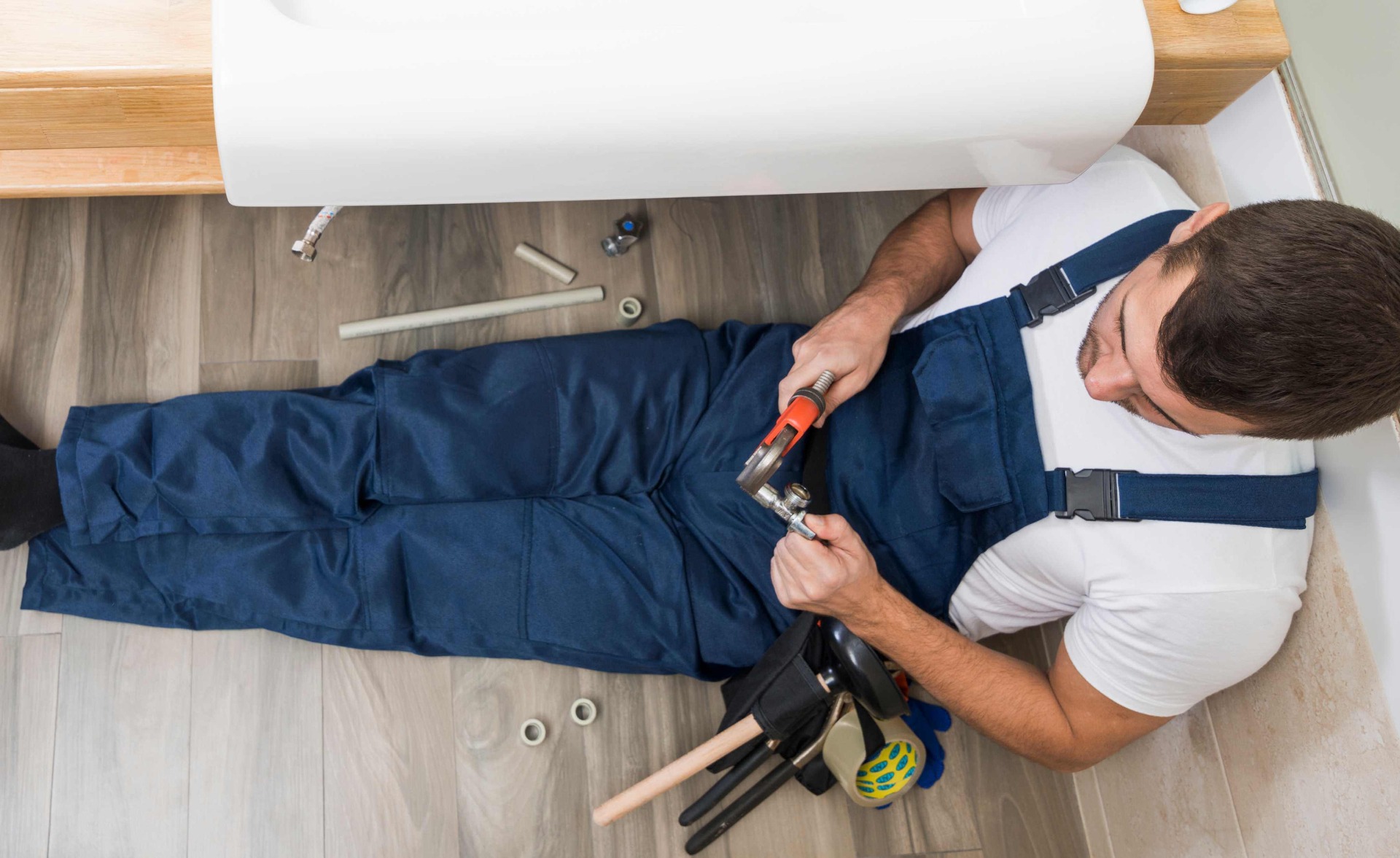 majstor koji leži na podu i zavrće maticu francuskim ključem